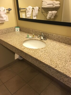 A bathroom with a granite countertop, a white sink, a mirror, and a towel rack with folded towels.