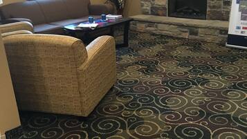 A living room with a stone fireplace, a television mounted on the wall, and a patterned carpet.