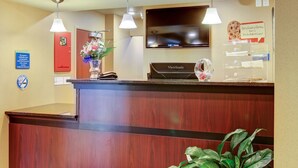 A hotel reception desk with a ViewSonic monitor, a flower vase, and a sign offering a fresh-baked cookie. - Travelodge by Wyndham Steele (Steele)