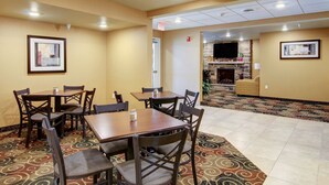 A hotel dining area with multiple tables and chairs, a patterned carpet, and a stone fireplace in the background. - Travelodge by Wyndham Steele (Steele)
