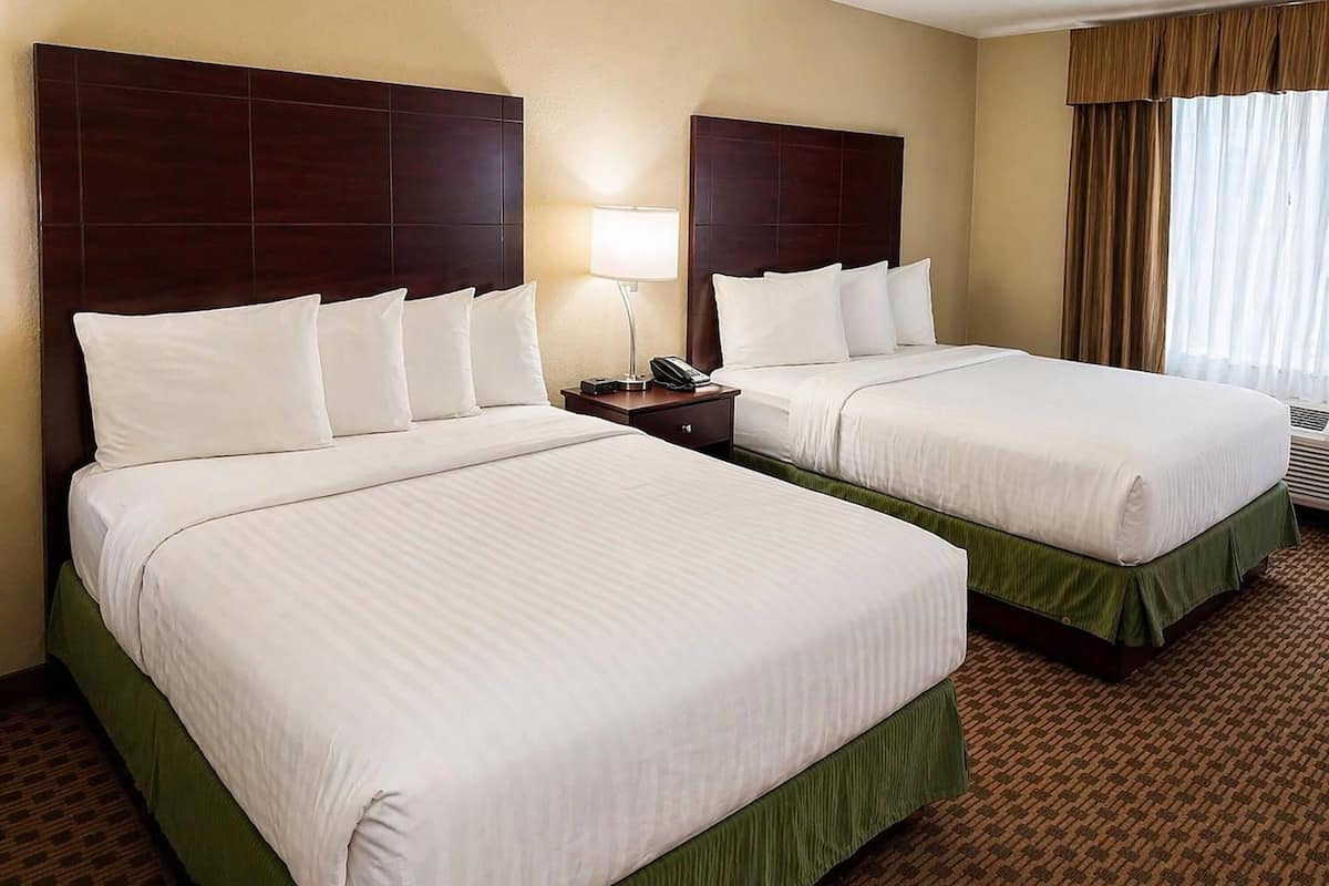 A hotel room with two beds, a nightstand with a lamp, and a window with curtains.
