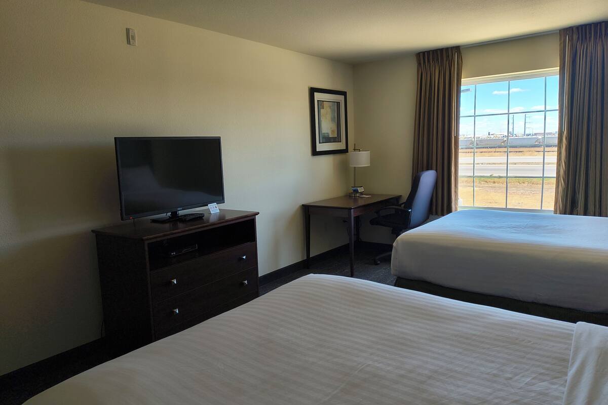 A hotel room with two beds, a TV on a dresser, a desk with a chair, and a window with curtains.
