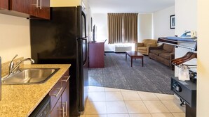 A compact hotel room with a kitchenette, a seating area with a sofa and armchairs, and a small dining table. - Cobblestone Inn & Suites - Eaton (Eaton)