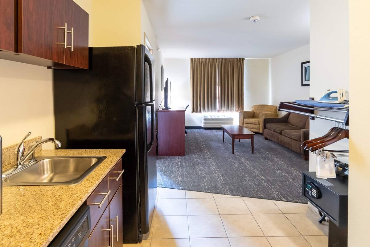A compact hotel room with a kitchenette, a seating area with a sofa and armchairs, and a small dining table.