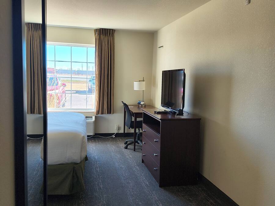 Ein Hotelzimmer mit Bett, Schreibtisch, Stuhl, Fernseher und einem Fenster mit Vorhängen.