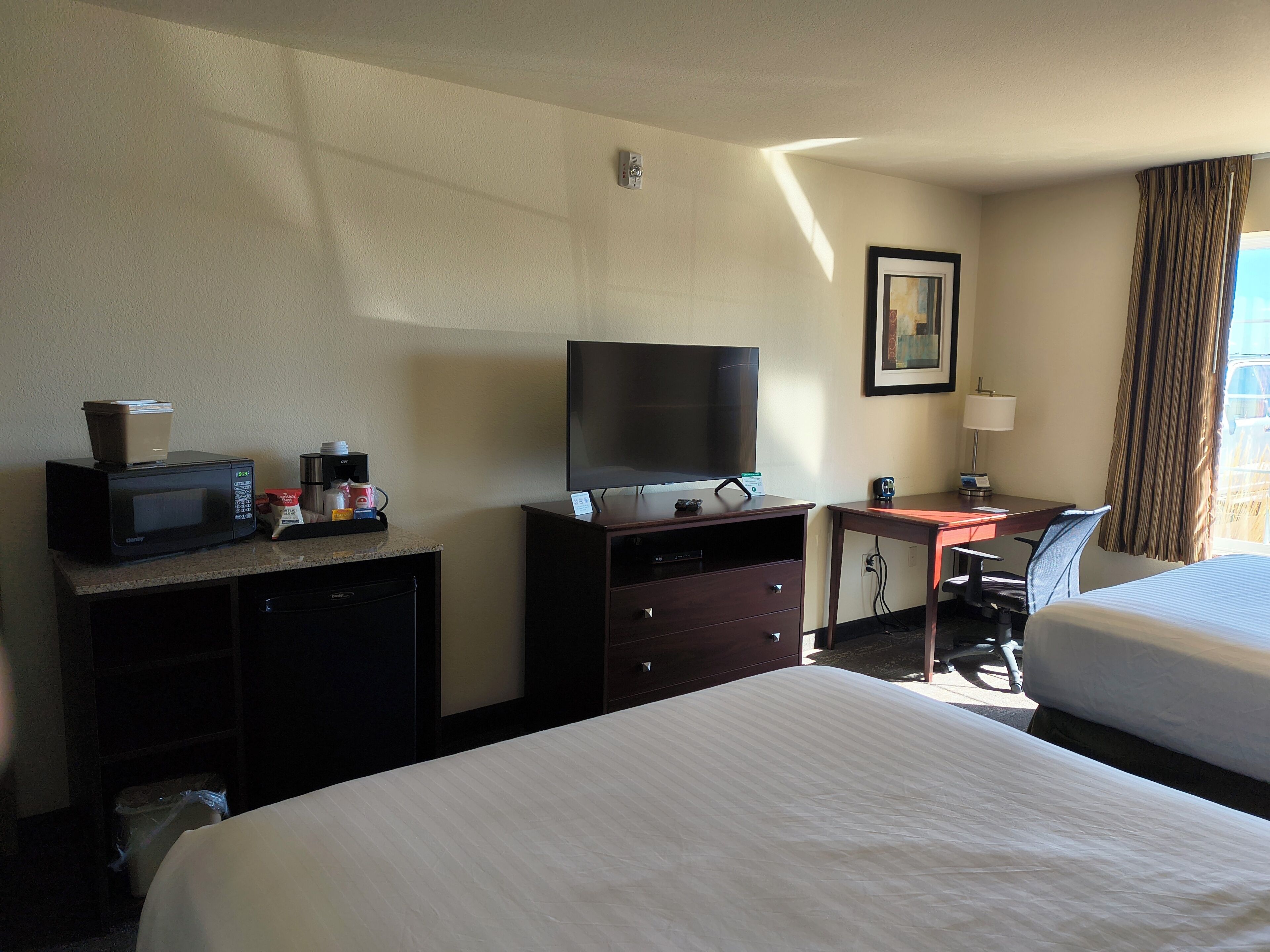 A hotel room with a bed, a desk with a computer, a television, a microwave, and a coffee maker.
