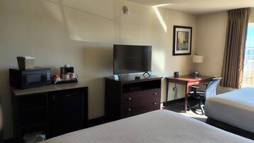 A hotel room with a bed, a desk with a computer, a television, a microwave, and a coffee maker.
