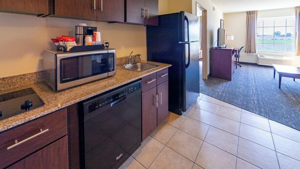 A modern kitchen with a dishwasher, microwave, refrigerator, and a dining area with a table and chairs. - Cobblestone Inn & Suites - Eaton (Eaton)