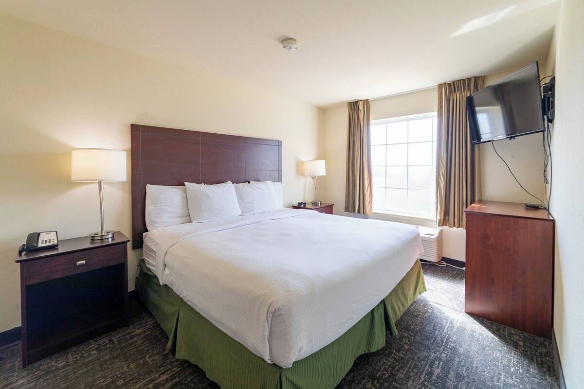 A hotel room with a large bed, two bedside tables, a flat-screen TV, and a window with curtains.