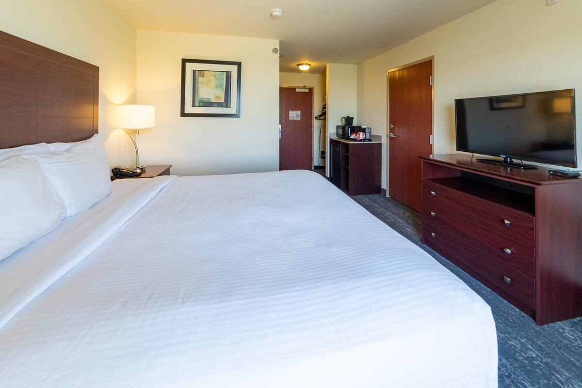 A hotel room with a large bed, a television, a desk with a lamp, and a wardrobe.