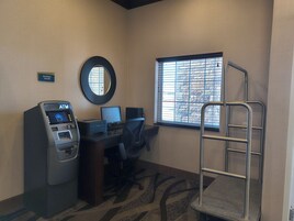 Centro de negocios con cajero automático, computadora y ventana con persianas.