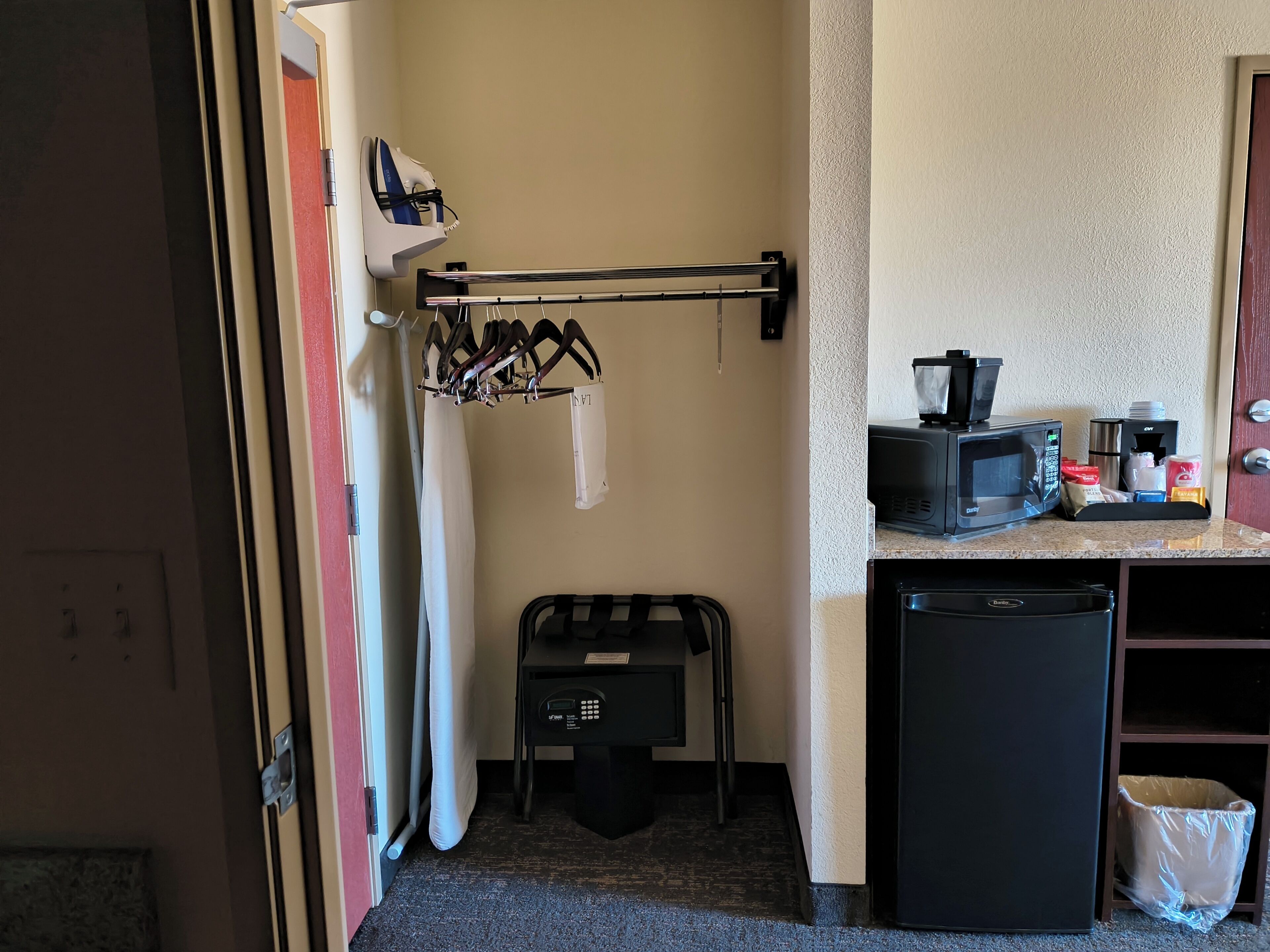 A compact hotel room with a kitchenette, a drying rack, a microwave, and a small trash bin.