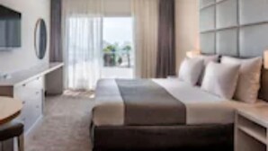 A modern hotel room with a large bed, a TV, a desk, and a view of the outdoors. - Astral Nirvana Suites (Eilat)