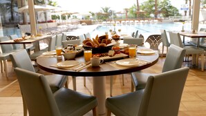 A dining area with a pool view, featuring a table set with breakfast items, chairs, and a view of the pool and palm trees. - Astral Nirvana Suites (Eilat)
