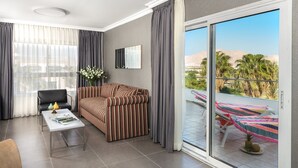 A modern living room with a striped sofa, a coffee table, and a dining table. There is a balcony with a pool table and lounge chairs. - Astral Nirvana Suites (Eilat)