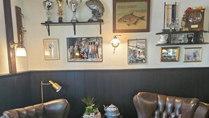 A cozy room with two leather armchairs, a small table with a plant, and a wall decorated with trophies, framed pictures, and a fish painting. - Hotel Arcense Herberg (Arcen)