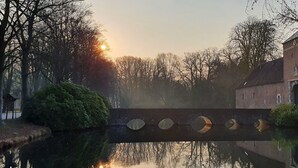 A canal with a bridge, trees, and a building with a tower. - Hotel Arcense Herberg (Arcen)