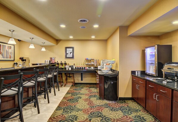 Una cocina de hotel con una zona de bar, taburetes, un cubo de basura y un refrigerador.