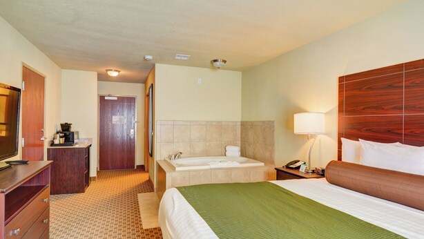Habitación de hotel con cama, escritorio, televisor y baño con bañera, además de un cabecero de madera.