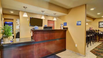 A hotel reception area with a wooden reception desk, a flat-screen TV, and a digital kiosk.