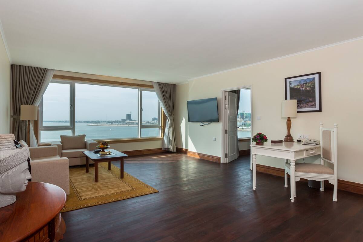 Habitación de hotel con un ventanal grande, un sofá, un escritorio, una silla, un televisor y una estatua.