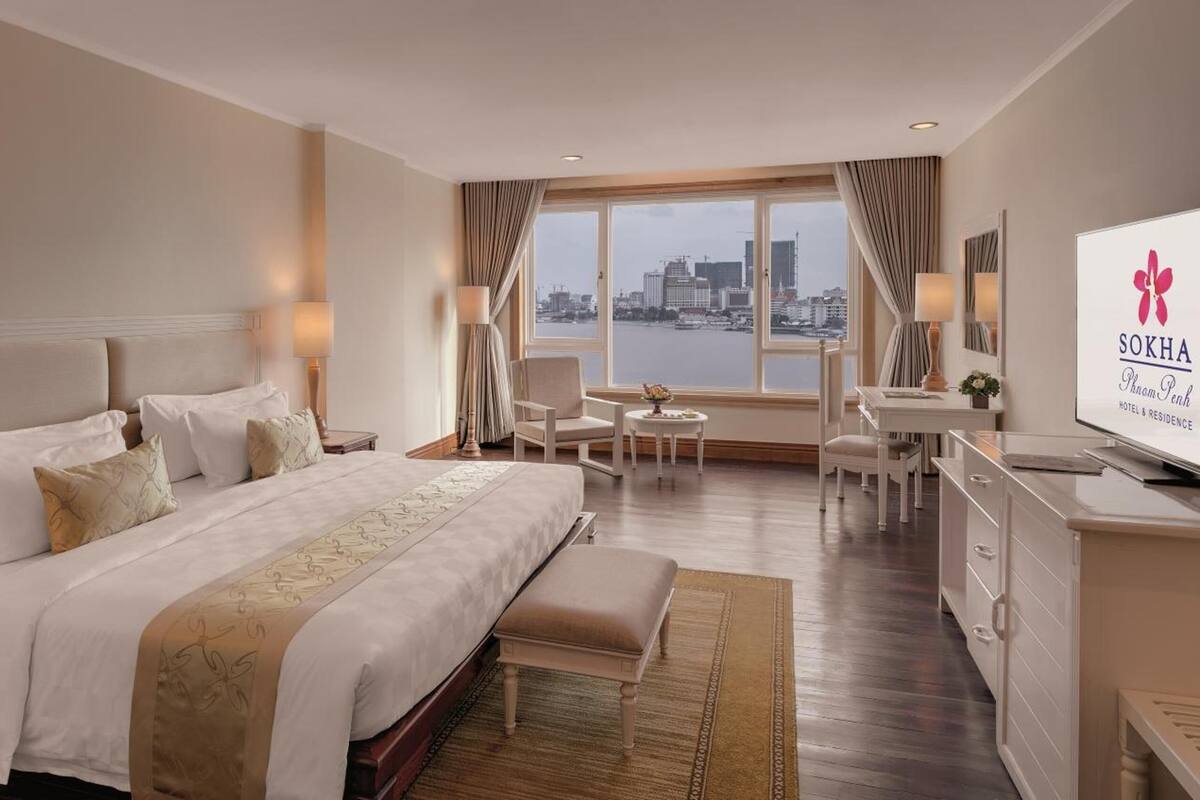 Habitación de hotel con una cama grande, un escritorio, una silla, un televisor y vistas a la ciudad desde la ventana.