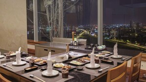 Una mesa de comedor dispuesta con varios platos y cubiertos, una botella de vino y vistas de un paisaje urbano nocturno.