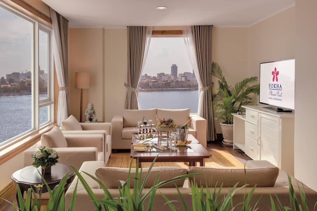 Una habitación de hotel moderna con vistas a la ciudad, un sofá, una mesa baja con aperitivos y un televisor en la pared.
