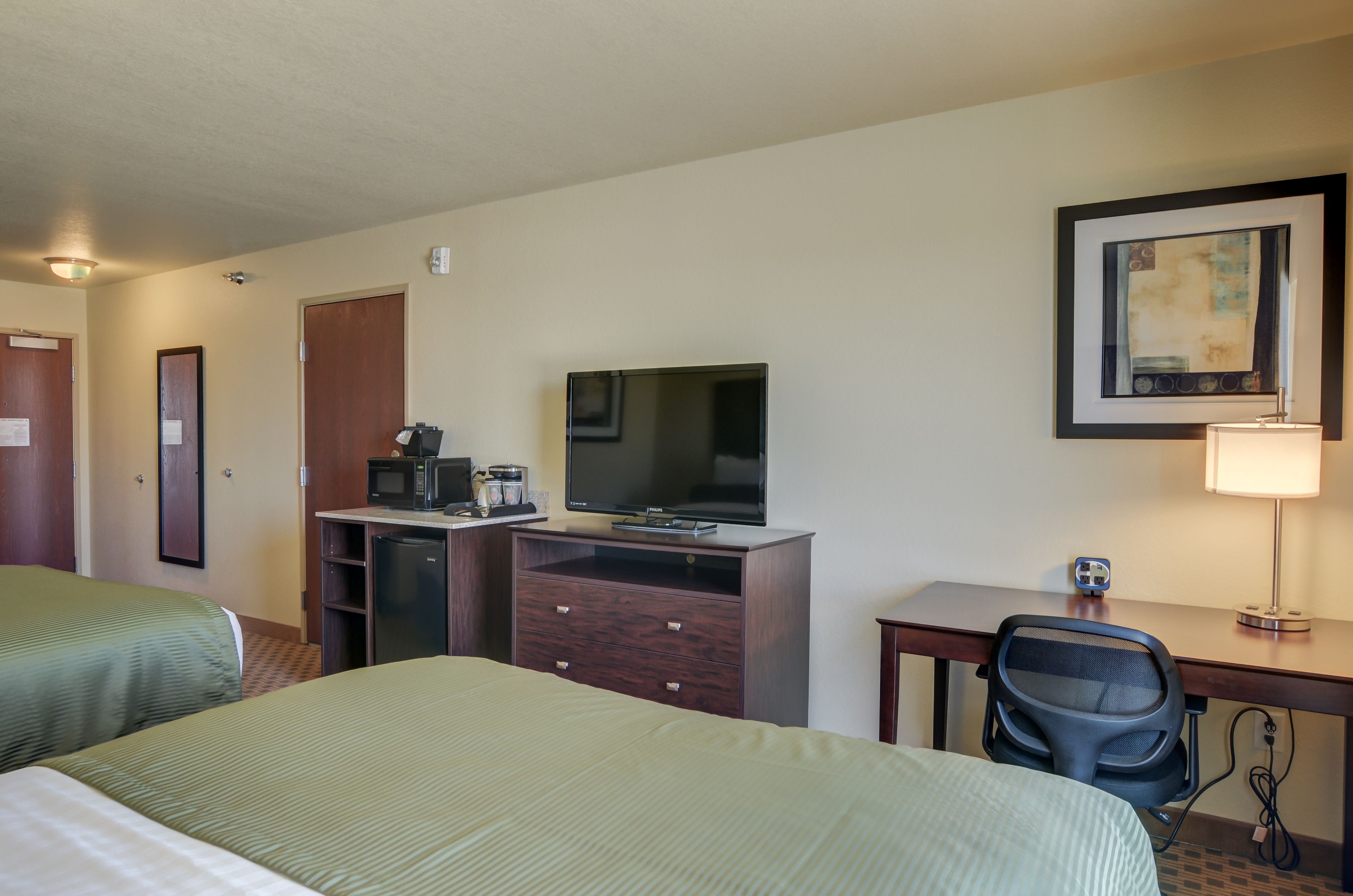 A hotel room with two beds, a desk with a lamp, a TV, a microwave, and a coffee maker.