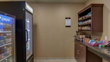 A kitchen area with a refrigerator stocked with beverages, a pantry with various food items, and a counter with snacks.