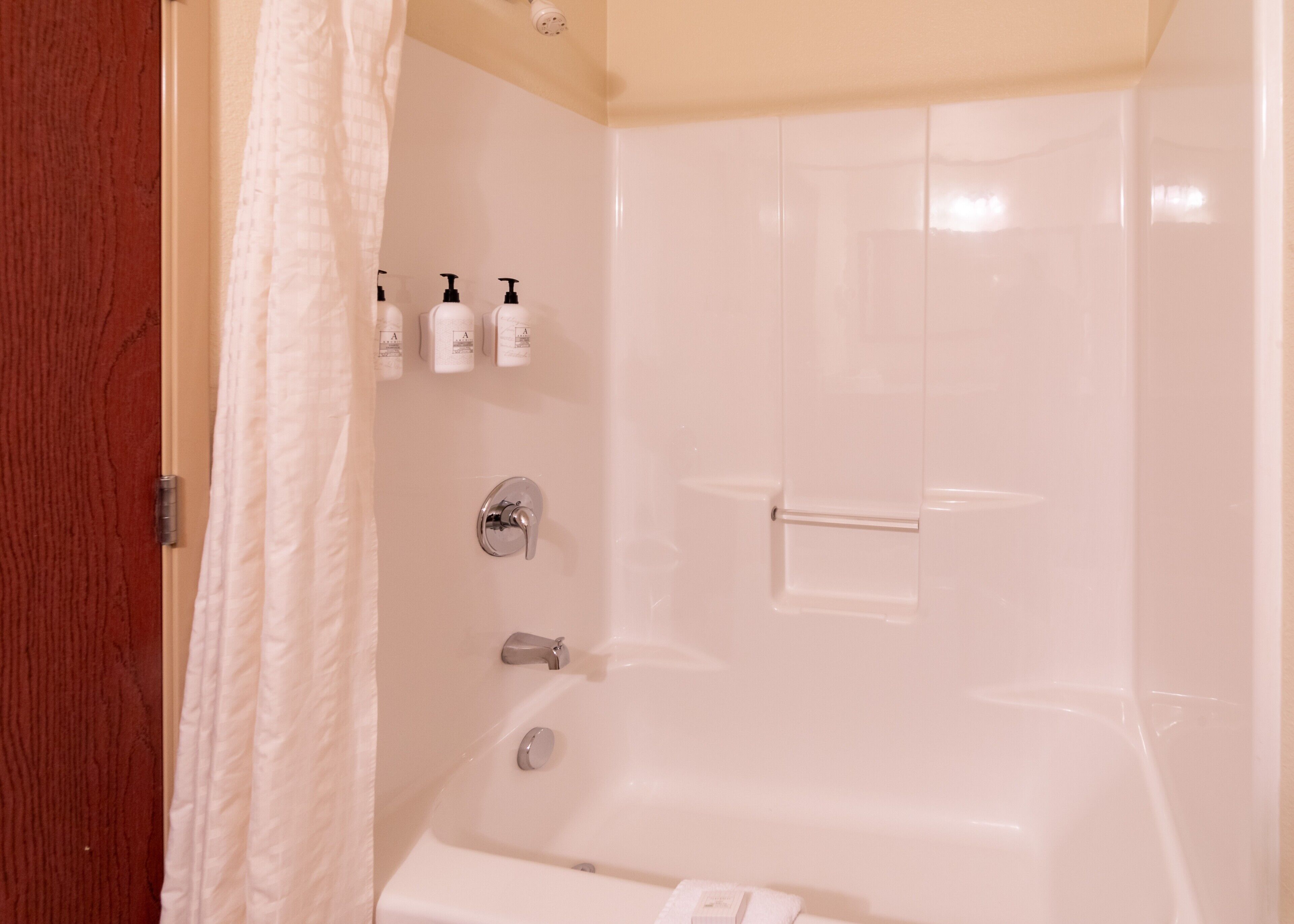 A bathroom with a bathtub, a shower, and a toilet. There are three bottles of shampoo on the wall.