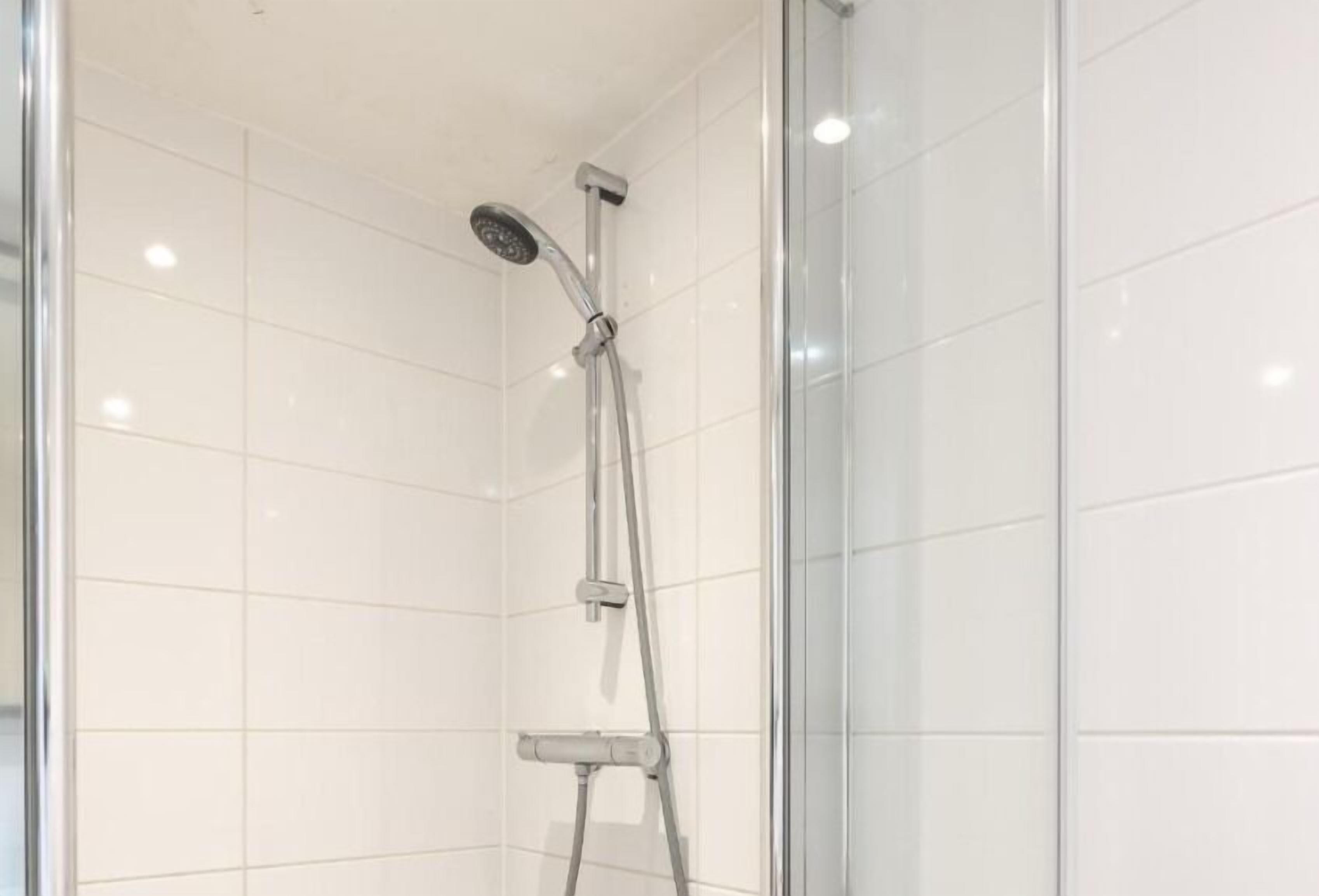 Une douche fermée par des parois en verre, dotée d’un pommeau de douche à main et d’un robinet fixé au mur.