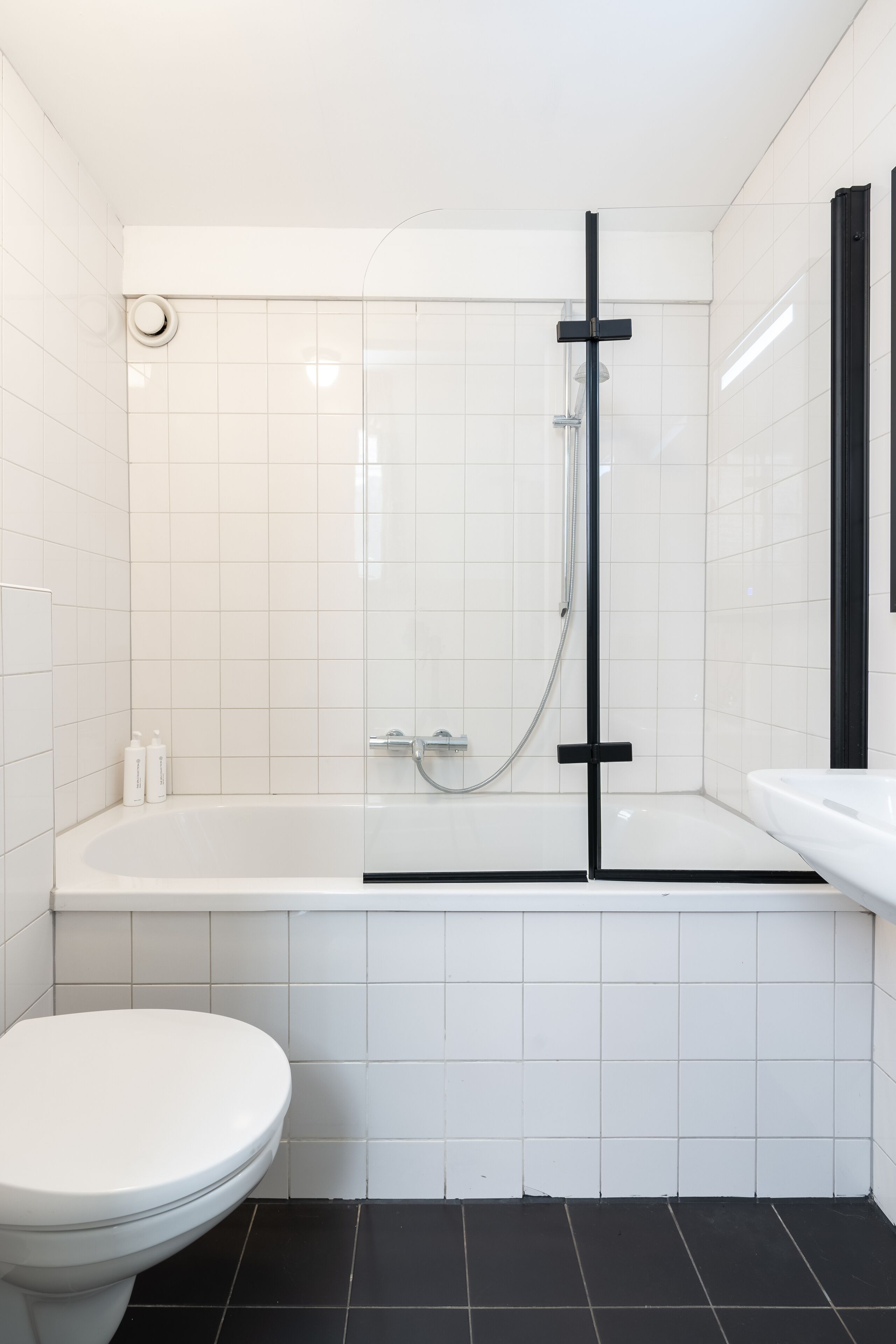 A modern bathroom with a white toilet, a glass-enclosed shower, and a black bathtub.