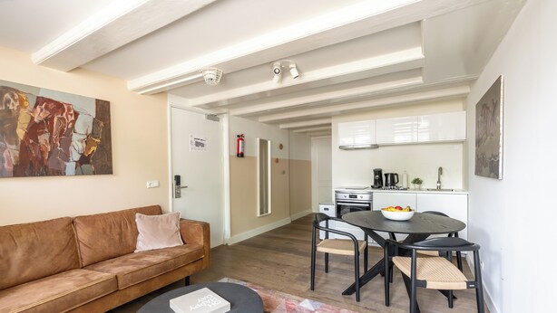 A modern living room with a brown leather sofa, a black ottoman, and a dining area with a black table and chairs. - Amsterdam Dockside Flats (Amsterdam)