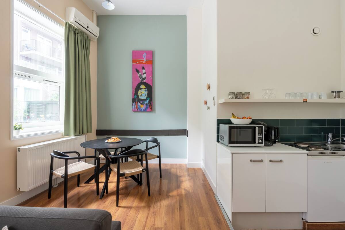 A compact kitchen with a dining area, a microwave, a stove, and a window with curtains.