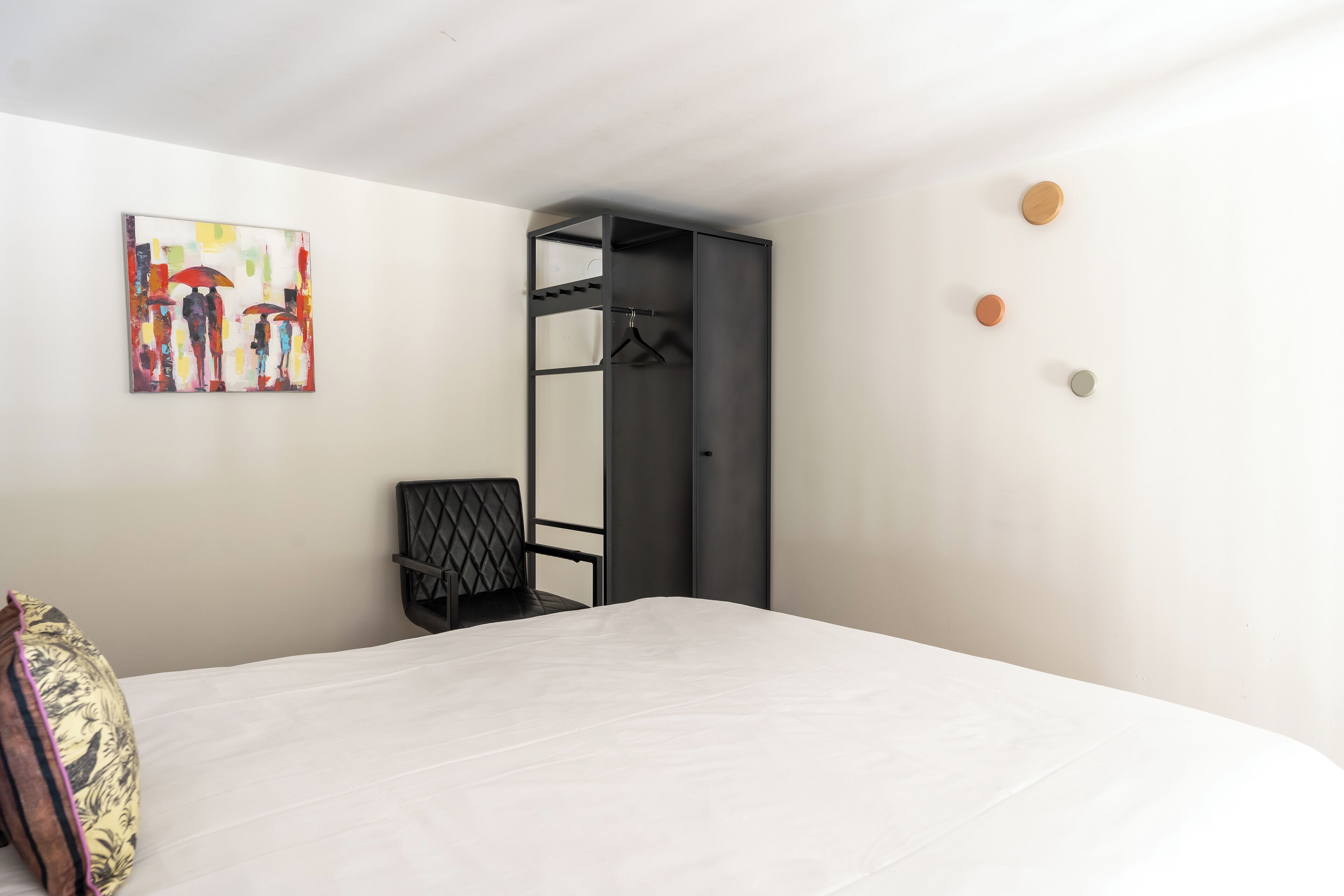 A bedroom with a bed, a chair, a wardrobe, and a painting on the wall.