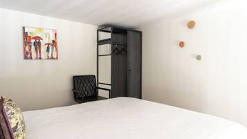 A bedroom with a bed, a chair, a wardrobe, and a painting on the wall.