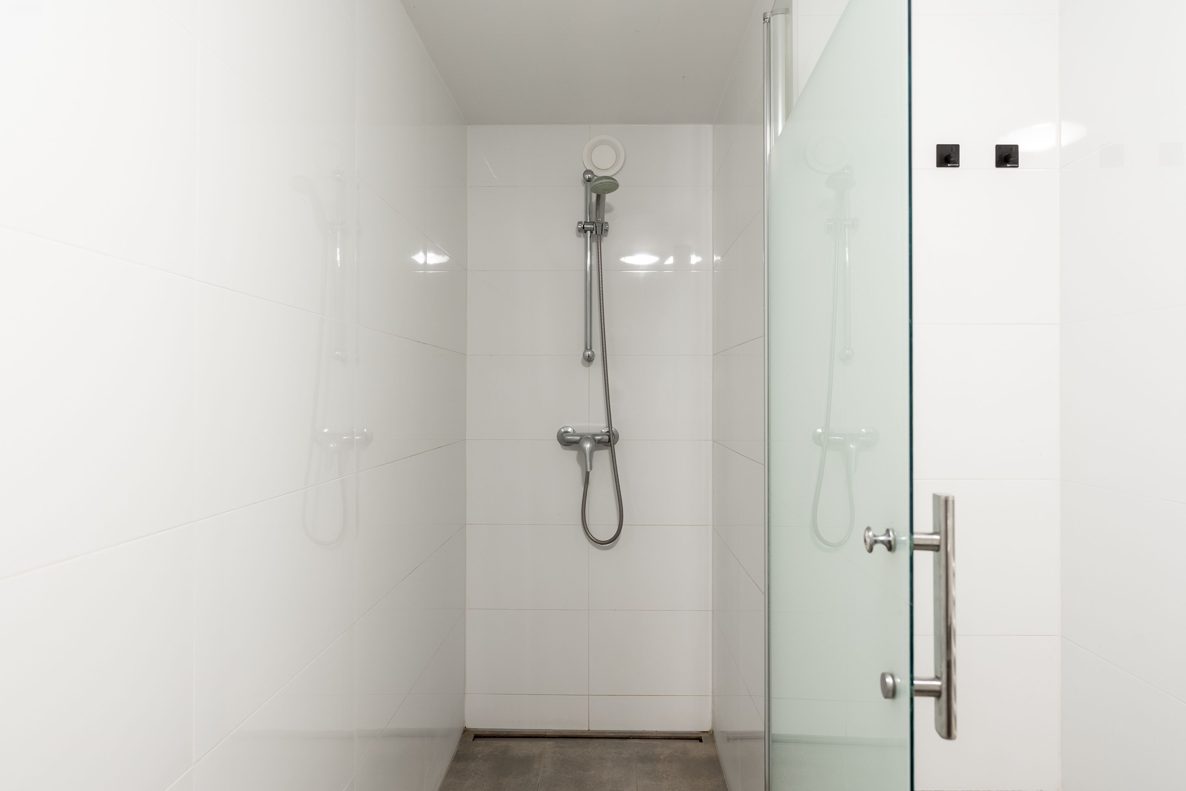A modern bathroom with a glass shower enclosure, a separate showerhead, and a glass door.