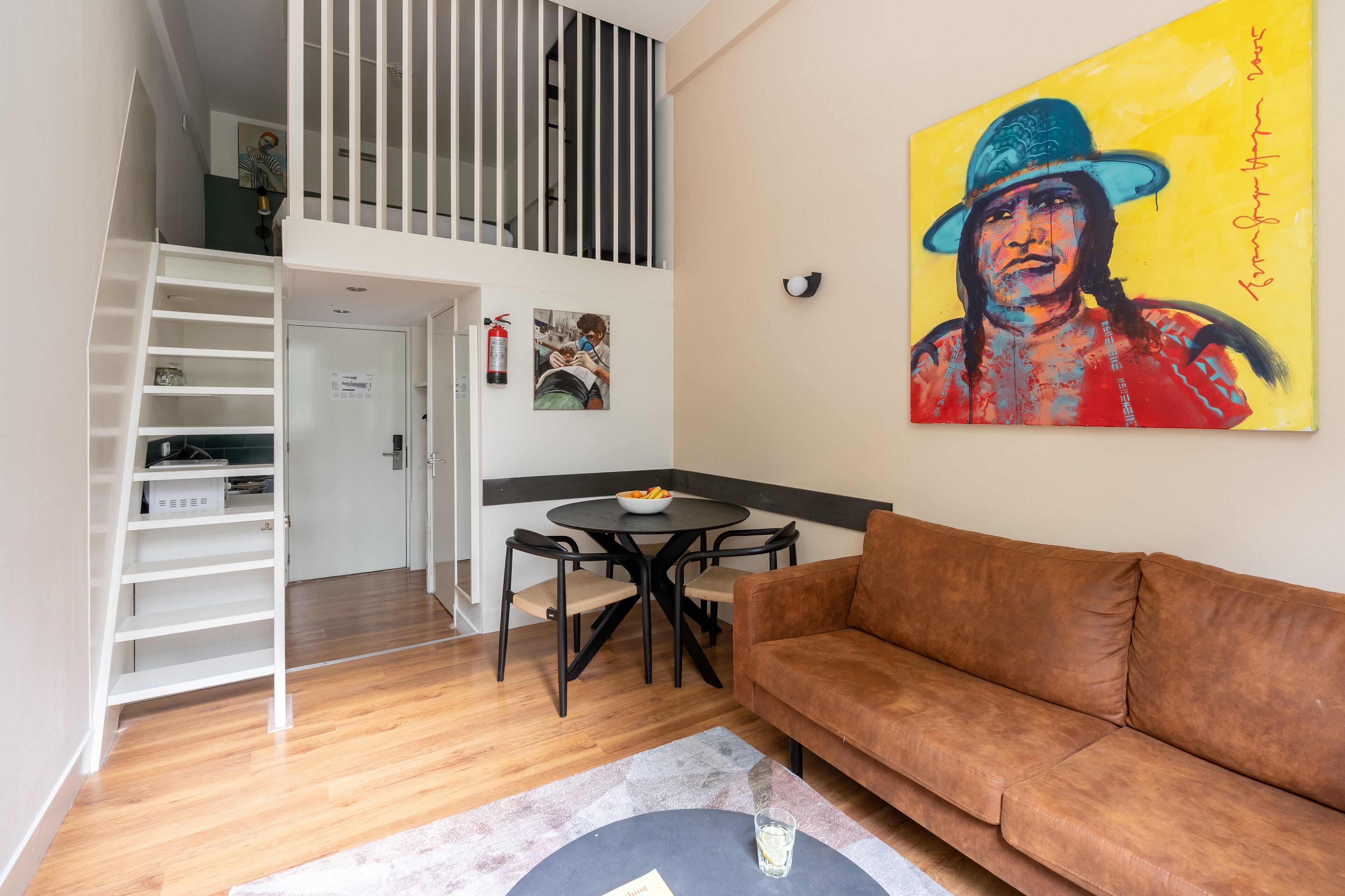 Un salon moderne avec un canapé marron, une table à manger avec des chaises, un escalier et un tableau accroché au mur.