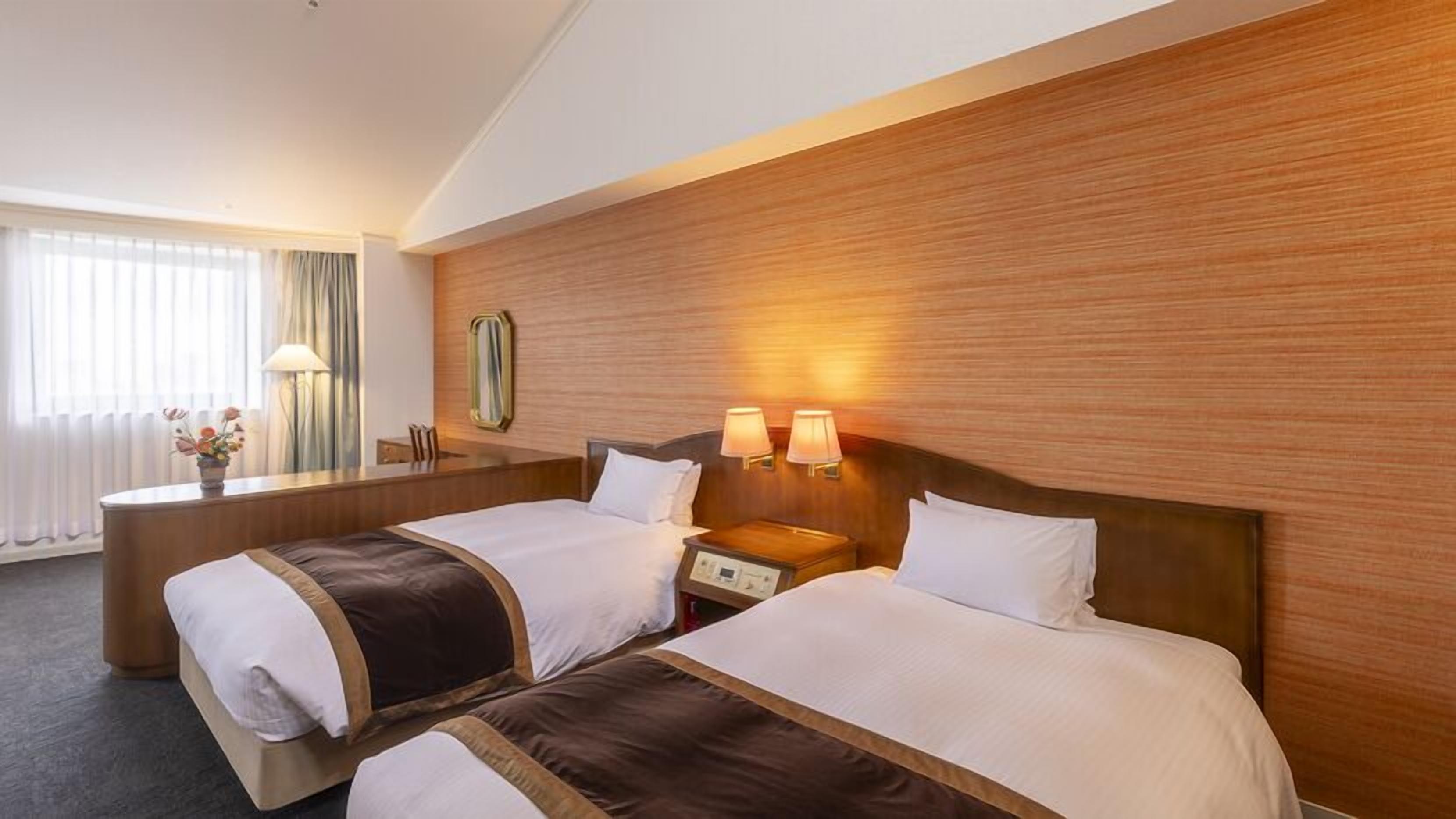 A hotel room with two beds, a desk, and a mirror.