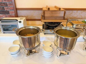 Een buffetopstelling met twee grote metalen potten, diverse witte kommen en een toaster.