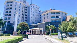 A multi-story hotel with a central courtyard, a parking area, and a clear blue sky.