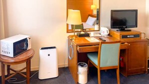 A hotel room with a wooden desk, a television, a microwave, a trash bin, and a chair.