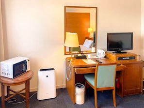 Ein Hotelzimmer mit einem Holztisch, einem Fernseher, einer Mikrowelle, einem Mülleimer und einem Sessel.