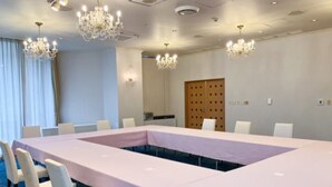 A conference room with a long table, white chairs, chandeliers, and a wooden door.