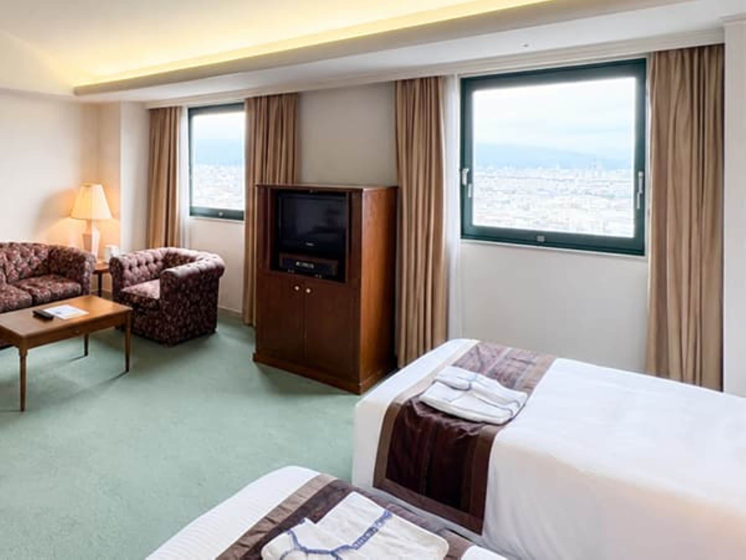 Une chambre d’hôtel avec un lit, un canapé, une télévision et une fenêtre donnant sur la ville.