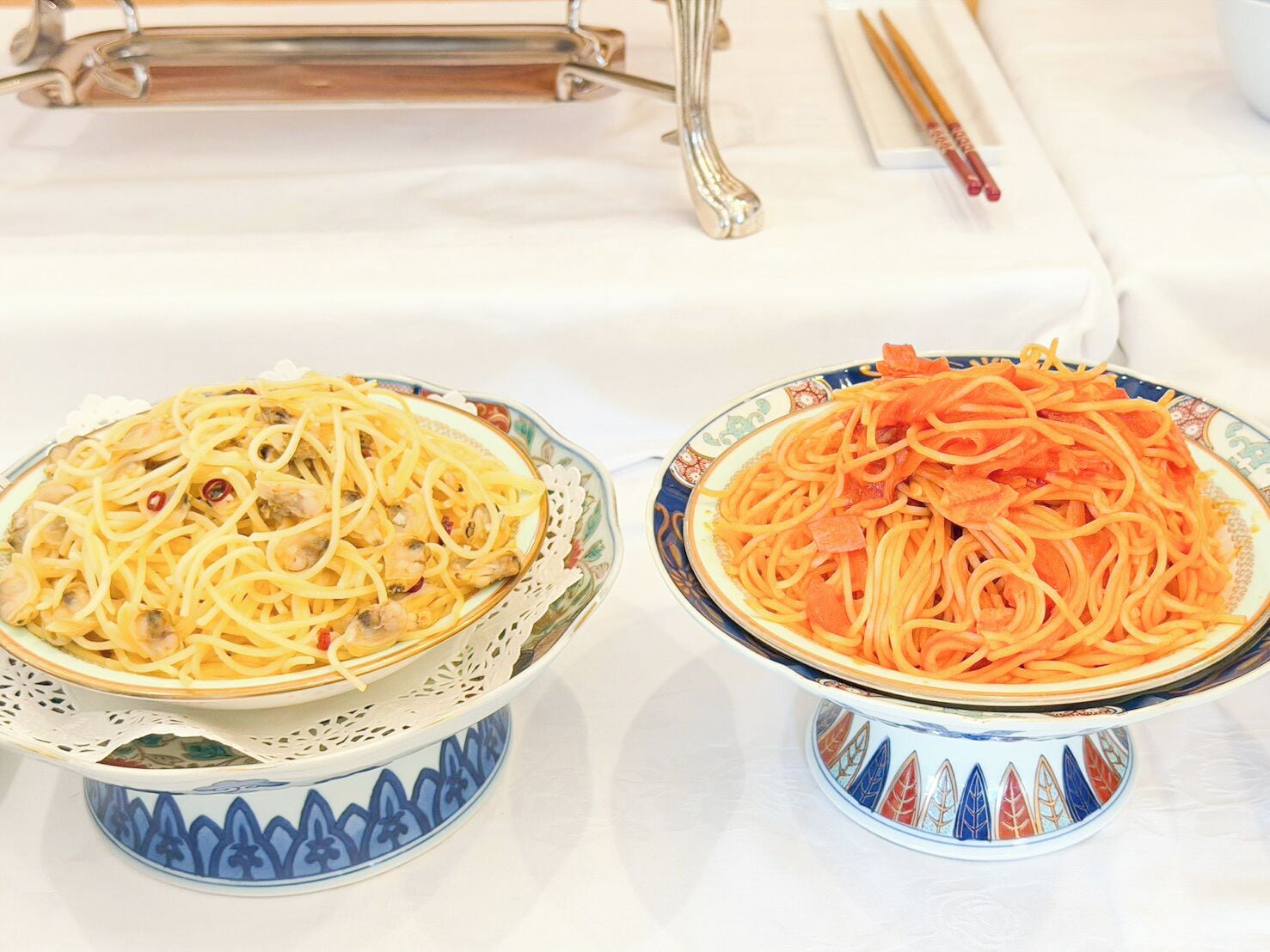 Two bowls of pasta on a table with chopsticks and a pair of glasses.