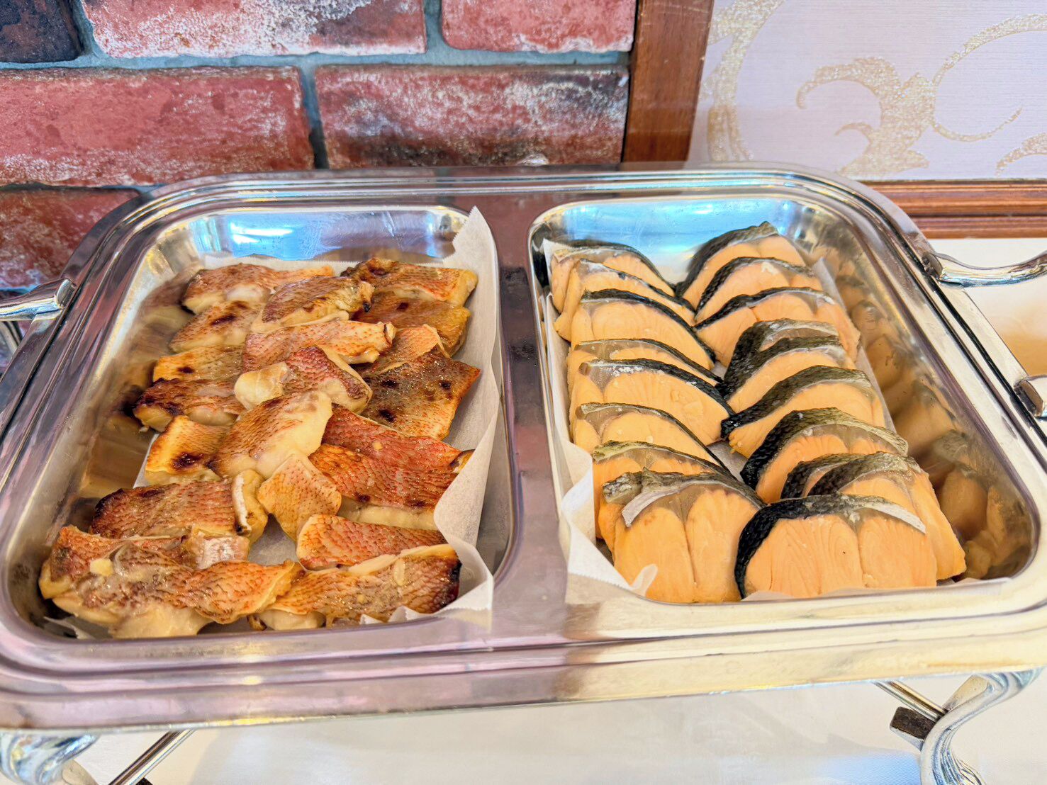 Ein Buffet mit zwei Speisenplatten, eine mit Aufschnitt und die andere mit Fisch.