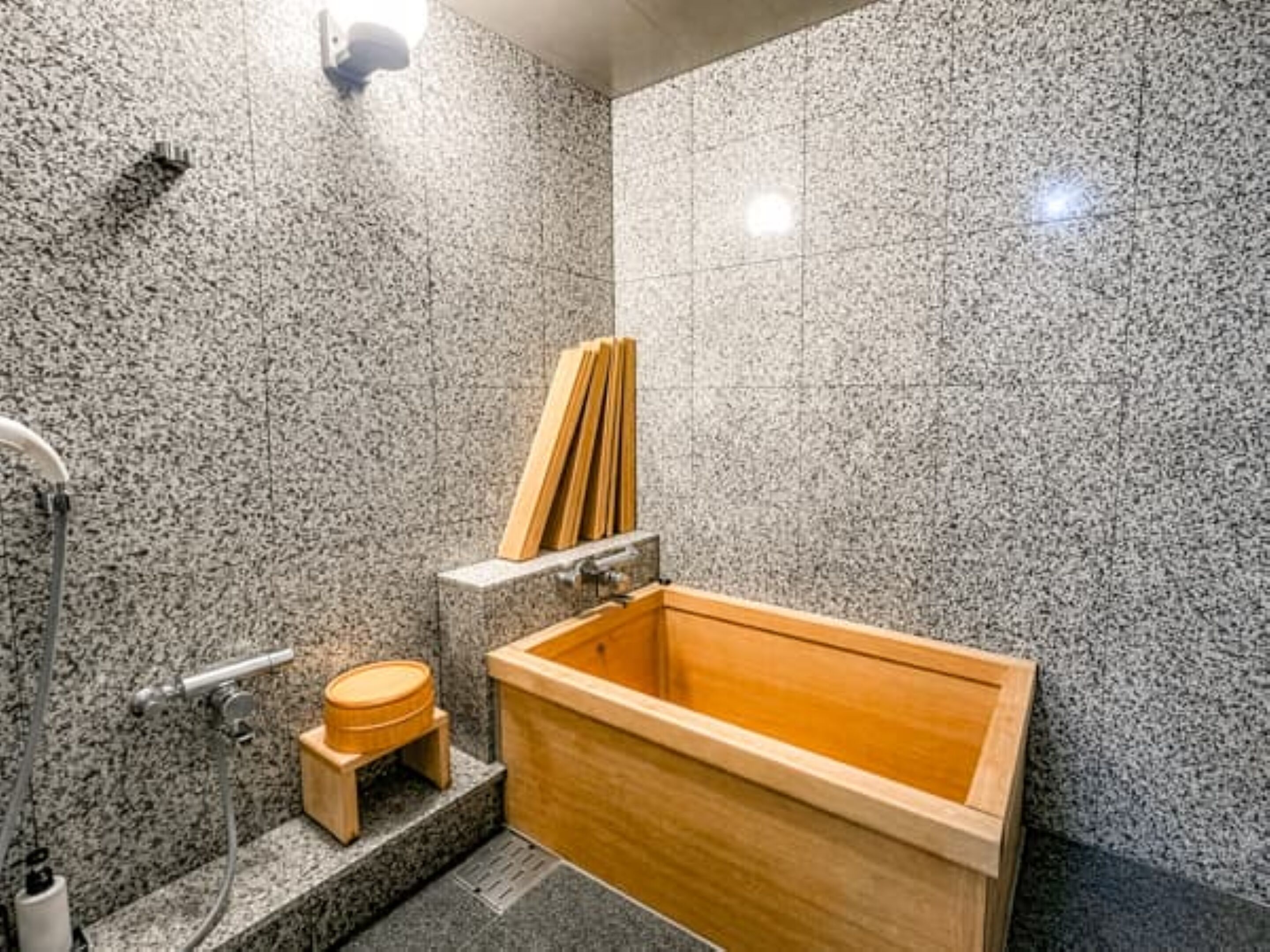 Une salle de bain de style japonais traditionnel, avec une baignoire en bois où l’on peut se prélasser, un petit tabouret en bois et un porte-serviettes.