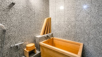 Une salle de bain de style japonais traditionnel, avec une baignoire en bois où l’on peut se prélasser, un petit tabouret en bois et un porte-serviettes.